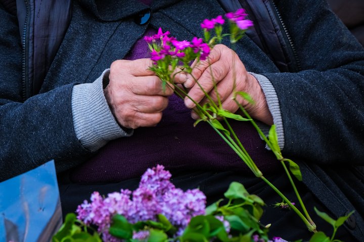 Violetines laukų gėles pina senyvos moters rankos.