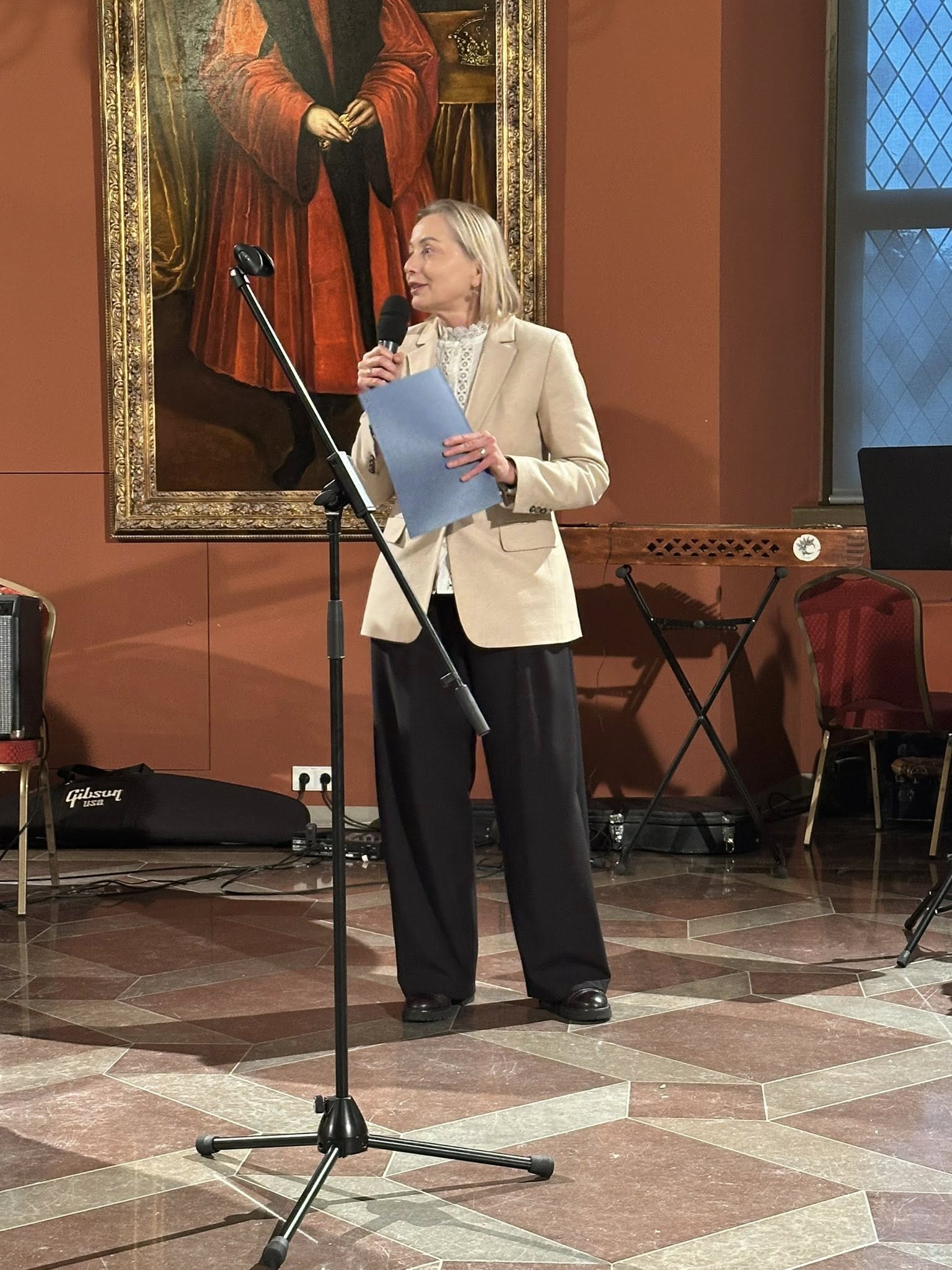 Agentūros vadovė E. Čaplikienė stovi su mikrofonu, sako sveikinimo žodį, rankoje laiko padėką.